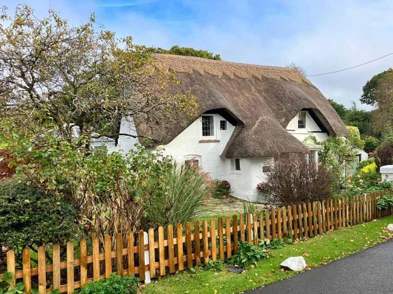 A thatched cottage, fencing, blue sky
