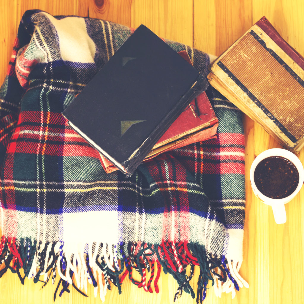 Woolen plaid, cup of coffee, old books on wooden background.