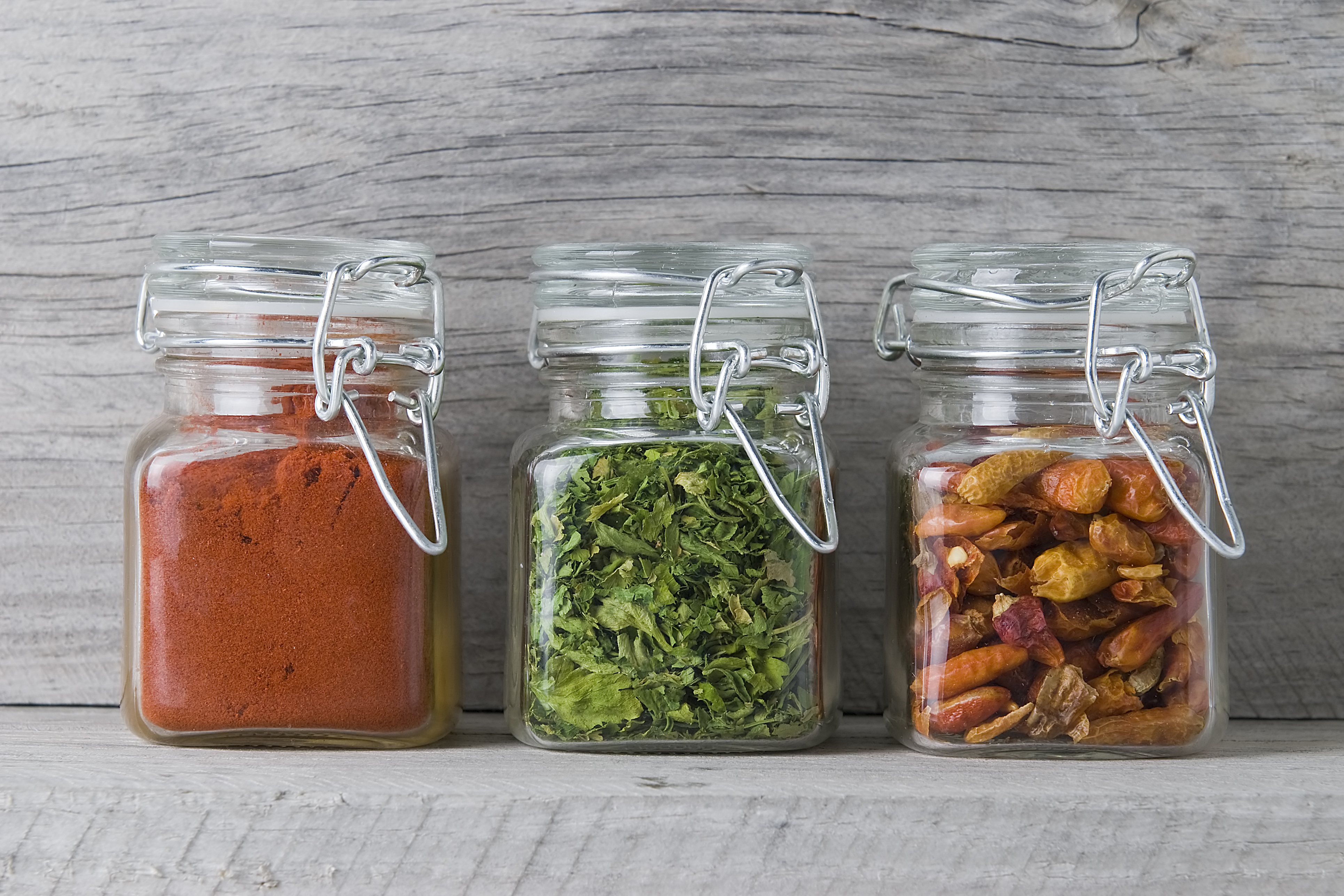Three jars with paprika, parsley and chilli on an old wooden spice rack.